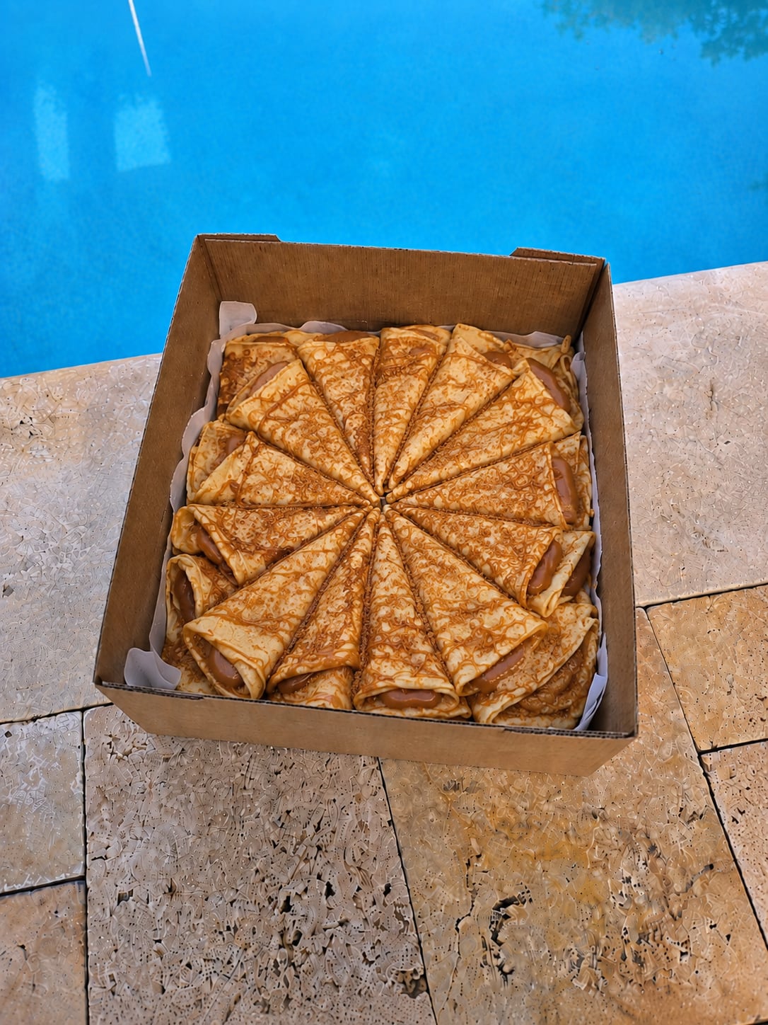 Caramel-filled French crêpes arranged in a wheel beside a pool