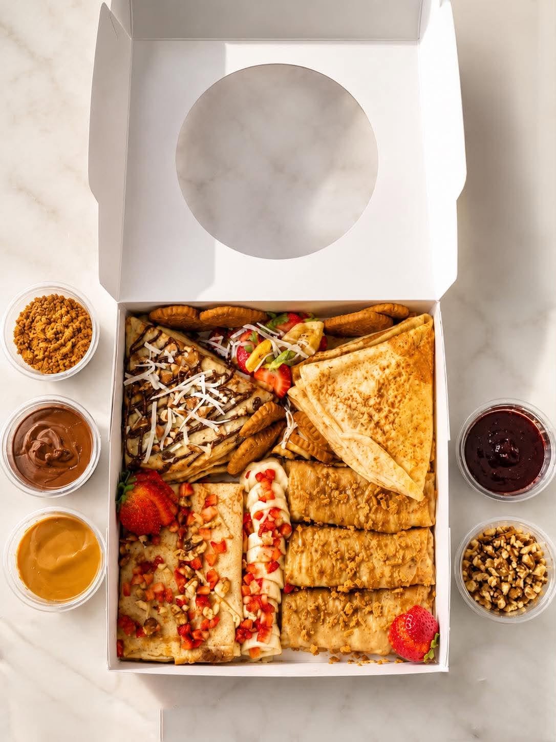 Overhead view of a LOCO Crêpes party box surrounded by sauces and crunchy toppings