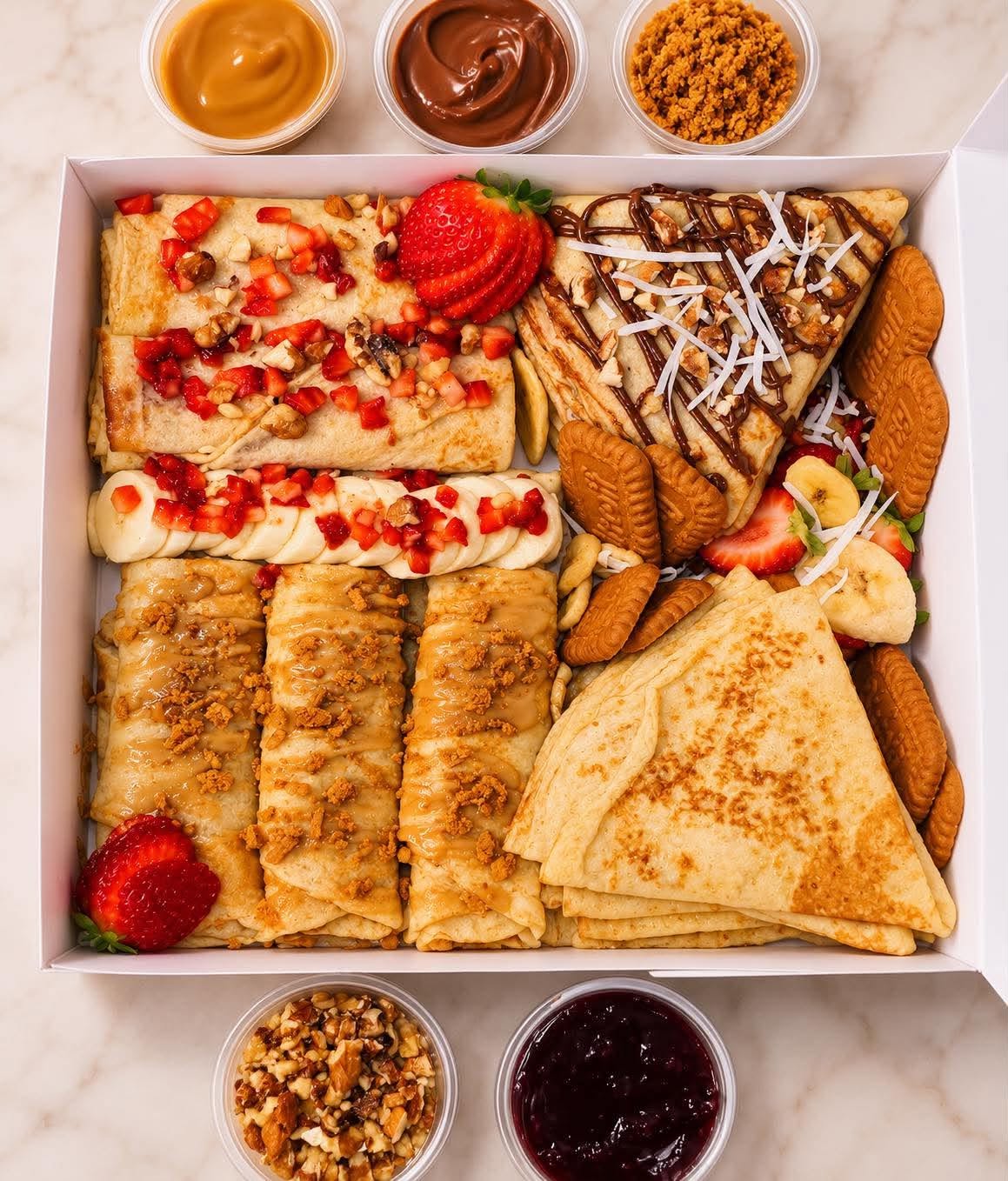 Close overhead view of assorted French crêpes with Nutella, fruit, Biscoff, and dipping sauces