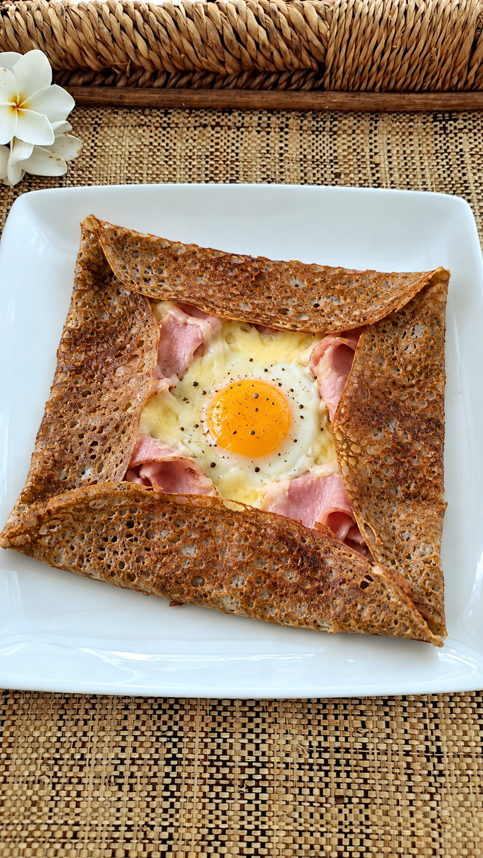 A Breton buckwheat galette with ham, cheese and egg on a white plate